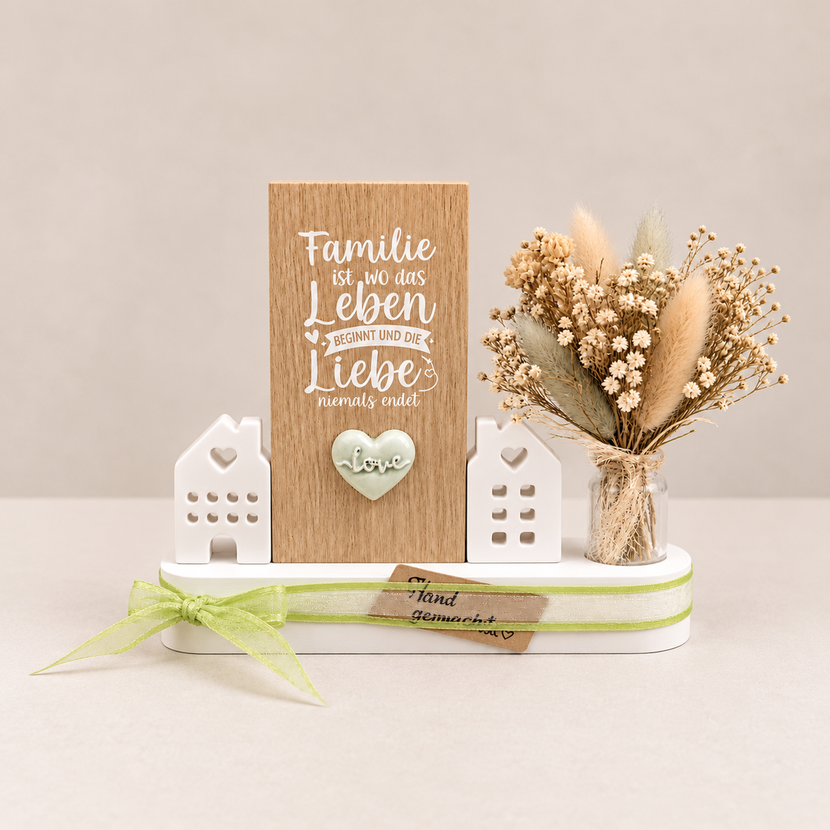 Familie ist – Holzschild mit Herz, weißen Dekohäusern, Trockenblumen und hellgrüner Schleife
